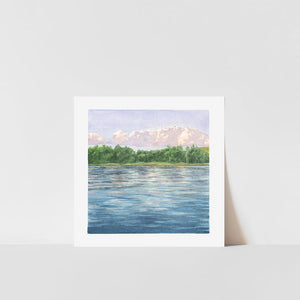 A framed art print depicting a landscape with a lake reflecting a blue sky, set against a white background.