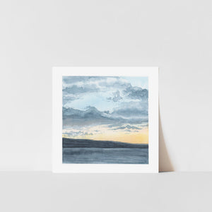 A framed art print depicting a lakeside sunset with a landscape in the background, displayed against a white backdrop.